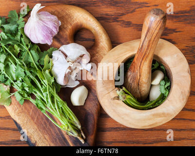 Kochen Gewürze - Draufsicht des hölzernen Mörser mit Koriander-Kraut und Knoblauch auf Tisch Stockfoto
