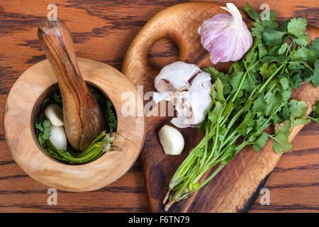 Kochen Gewürze - oben Blick auf hölzernen Mörser mit Koriander-Kraut und Knoblauch auf Tisch Stockfoto
