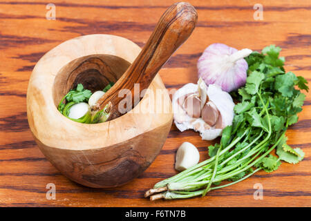 Kochen Gewürze - hölzerne Mörser mit Koriander Gras- und Knoblauch auf Tisch Stockfoto
