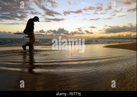 Fischer-Strand ist ein Fischer am Strand entlang spazieren, bei Sonnenaufgang Silhouette gegen den Wolkengebilde Himmel und steigende frühen Mo Stockfoto