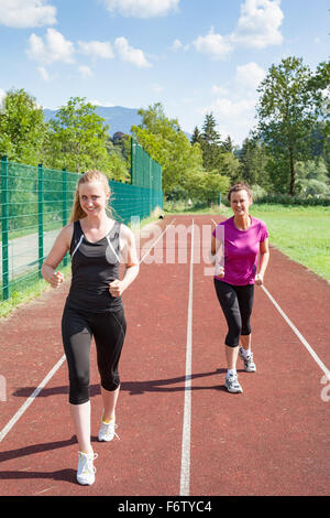 Zwei Frauen zusammen auf dem richtigen Weg laufen und Freundschaftsrennen - blonde Frau gegen Brünette Frau in Track-Rennen Stockfoto