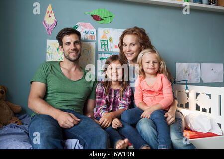 Familienbild des Paares mit ihren kleinen Töchtern sitzen zusammen auf dem Bett im Kinderzimmer Stockfoto