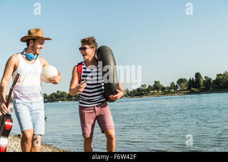 Zwei Freunde mit Innenrohr und Gitarre zu Fuß am Fluss Stockfoto