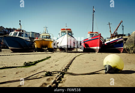 Fünf bunte Boote vertäut im Hafen bei Ebbe an einem sonnigen Nachmittag, Tenby, Pembrokeshire, Wales, UK. Stockfoto