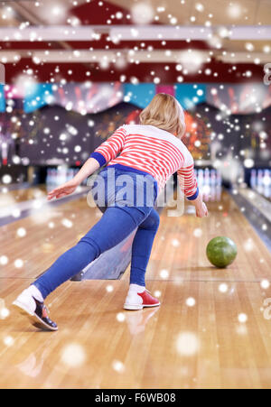 glückliche junge Frau wirft Ball in Bowlingclub Stockfoto