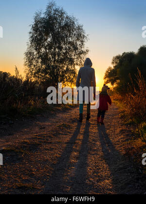 Mutter und Tochter gehen auf Landstraße bei Sonnenuntergang Stockfoto