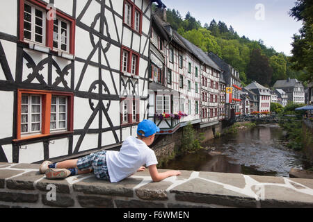 Junge liegend auf einer Brücke betrachtet man Fachwerkhäuser entlang der Rur, Monschau, Eifelsteig Wandern trail, Eifel, NRW-Westp Stockfoto