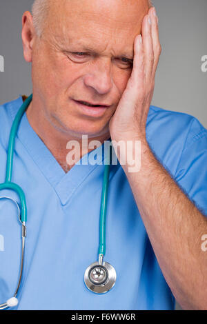 Verstört Arzt tragen blaue scheuert sich, mit seiner Hand auf seinem Kopf/Gesicht. Stockfoto