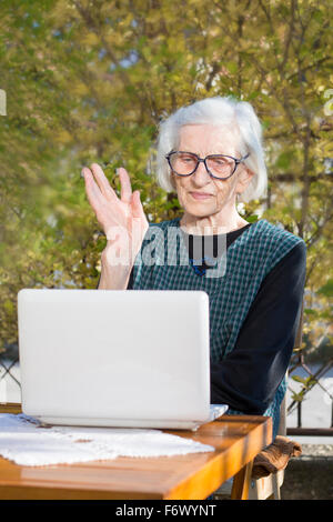 Ältere Frau, die einen Videoanruf auf einem Notebook-Computer im Hinterhof Stockfoto