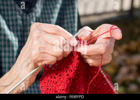 Alte Frau die Hände einen roten Pullover stricken, für ein Weihnachtsgeschenk Stockfoto