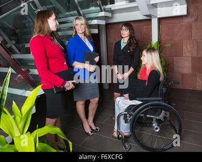 Vier professionelle Business-Frauen in der Lobby eines Büros, eines davon querschnittsgelähmt im Rollstuhl ist; St. Albert, AB, CA Stockfoto