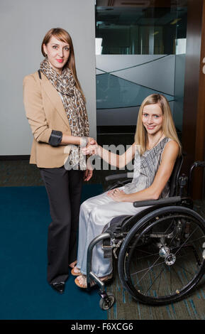 Eine professionelle Business-Frau, Hände schütteln und posiert mit einer jungen Frau der querschnittsgelähmt im Rollstuhl; St. Albert, Alberta, CA Stockfoto