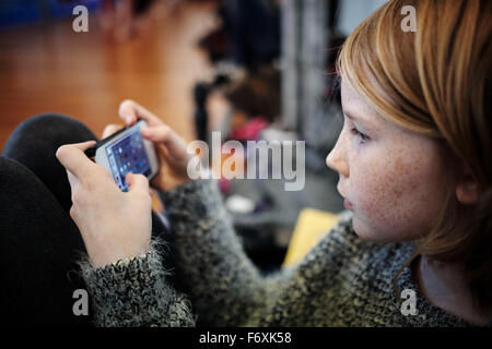 Junge blonde Mädchen spielen auf Handy-Gerät Stockfoto