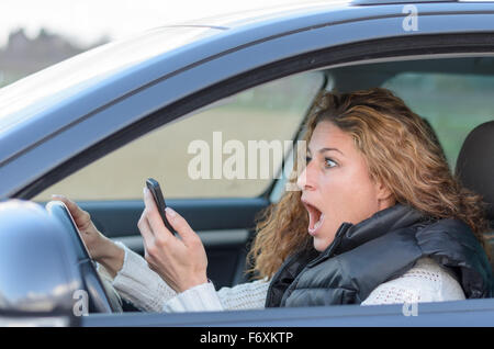 Frau schockiert ist ihr Auto zu fahren und auf der Suche auf ihrem Handy Stockfoto