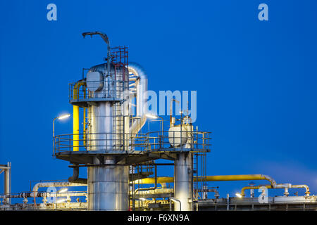 Detail eines Destillationaufsatzes einer Chemiefabrik und Raffinerie mit blauen Nachthimmel und Beleuchtung. Stockfoto