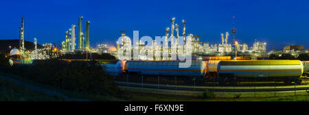 Panoramablick auf eine Chemiefabrik und Raffinerie mit blauen Nachthimmel und Beleuchtung, einige Güterzüge im Vordergrund. Stockfoto