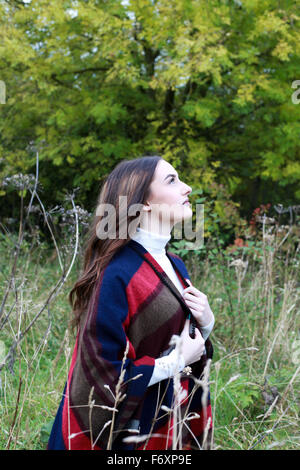 Profil von Aufnahme einer jungen Frau blickte zum Himmel ansehen in einem Feld mit Bäumen im Hintergrund Stockfoto