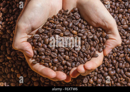 Hände eines Mannes hält eine Handvoll braunen Kaffeebohnen. Kaffeebohnen als einheitlichen Hintergrund. Stockfoto