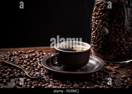 Kaffee-Tasse und Untertasse mit verstreuten Kaffeebohnen auf einem Holztisch Stockfoto