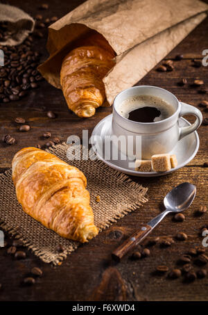 Kaffee und Croissant mit verstreuten Kaffeebohnen auf hölzernen Hintergrund Stockfoto