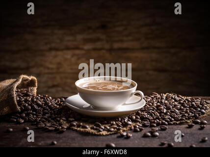 Tasse Kaffee mit verstreuten Kaffeebohnen auf hölzernen Hintergrund Stockfoto