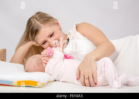 ein zwei-Monats-Baby liegend auf dem Rücken auf dem Bett sitzen neben dem Kind und die Mutter sah Sie Stockfoto