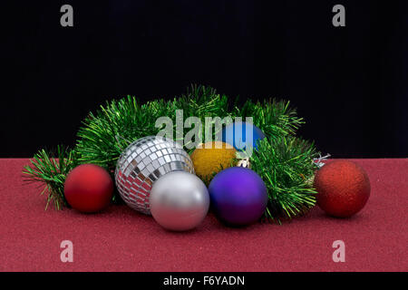 Weihnachtsvorbereitungen, Christbaumkugeln und Lametta auf glitzerndes rot und schwarz. Stockfoto
