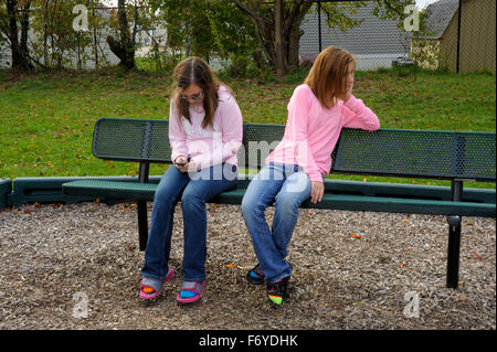 Zwei preteen Mädchen im Park. Ein Mädchen ignoriert wird, während das andere Mädchen auf Handy ist. Stockfoto