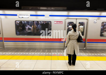 Eine japanische Frau wartet bei der Metro für einen vorbeifahrenden Zug Stockfoto