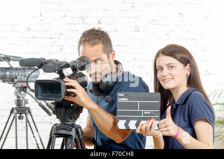 ein Lächeln auf den Lippen Kameramann und hübsche junge Frau mit einer Filmkamera und Klöppel Stockfoto