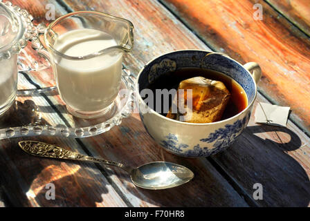 Tasse Tee in antike Tasse mit Milch und Zucker auf rustikalen Hintergrund Stockfoto