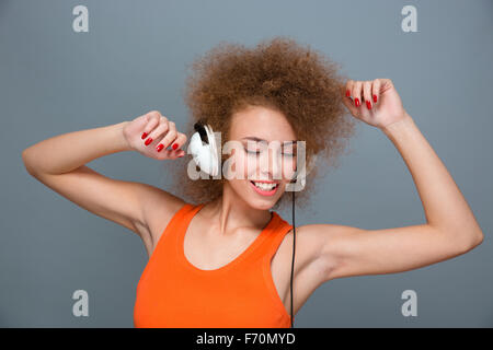 Positive lächelnde entspannte moderne schöne lockiges Mädchen in orange Top Musik hören und tanzen mit geschlossenen Augen Stockfoto