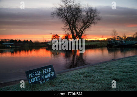 Rufford Marina, Burscough, Preston, Lancashire, Großbritannien, 23. November 2015. UK Wetter bei Sonnenaufgang. 'Bitte geben Sie Enten im Wasser'-Schild an einem kalten, frostigen und kühlen Start in den Tag mit einem Hausboot Bewohner auf der Leeds Liverpool canal Aufwachen zu einem herrlichen Sonnenaufgang. Die rufford Branch zwischen Rufford und Sollom wurde durch die Douglas Navigation um 1760 gebaut. Sieben Jahre nach dem Leeds & Liverpool Canal abgeschlossen wurde, ein Zweig von burscough zu Rufford, eröffnet im Jahr 1781. Der letzte Abschnitt, von sollom zu Tarleton, im Jahre 1805 als Teil des Croston Entwässerung Verbesserungen eröffnet. Stockfoto