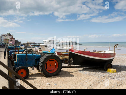 Traktoren und Angelboote/Fischerboote am Strand von Cromer, Norfolk, UK, mit Häusern und dem Pier in der Ferne. ungespitzten. Stockfoto