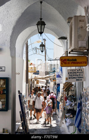 Santorini. Touristen zu Fuß durch die typischen engen gepflasterten Straße mit Geschäften auf beiden Seiten, im alten Stadtzentrum von Fira im heißen Sommer. Stockfoto