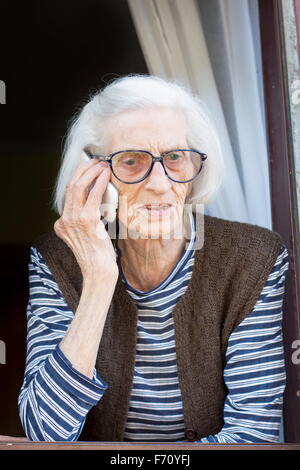 Alte Oma am Telefon auf ihrem home-Fenster stehend Stockfoto