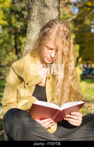 Blondes Mädchen in einem roten Buch in einem Park an einem sonnigen Tag Stockfoto