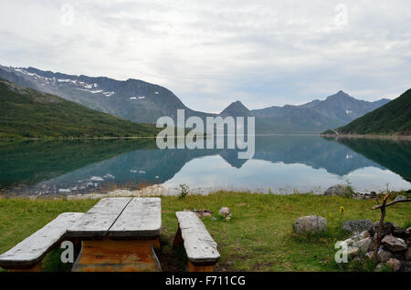 ruhigen Fjord umgeben von Bergen, im Sommer mit klaren Reflexion über Fjord Oberfläche mit hölzerne Parkbank und Feuerstelle Stockfoto