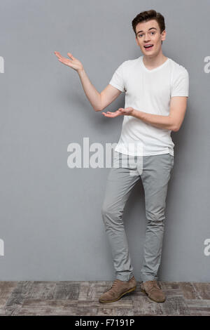 In voller Länge Portrait von attraktiven inspiriert glücklichen lächelnden lässigen jungen Mann in weißem T-shirt und grau Hose Exemplar festhalten Stockfoto
