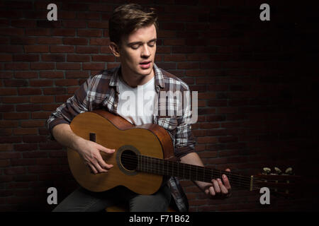 Handsome konzentriert ernsteren nachdenklichen jungen Mann im karierten Hemd akustische Gitarre spielen und singen Stockfoto