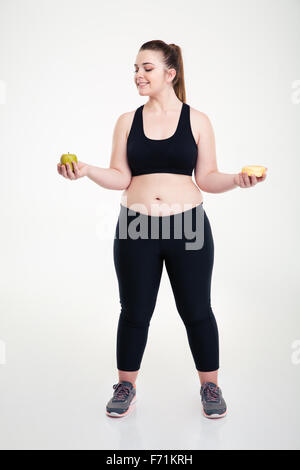 Voller Länge Porträt einer lächelnden Fette Frau die Wahl zwischen Donut und Apfel isoliert auf weißem Hintergrund Stockfoto