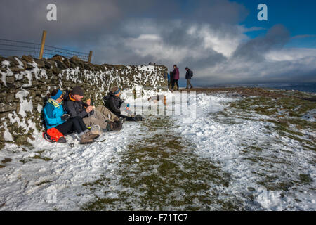 Haustiere: Leute genießen Schnee, Sonnenschein und Sandwiches auf dem Gipfel des Pen-y-Gent an einem verschneiten Tag, eines der berühmten Yorkshire Drei Zinnen Berge Stockfoto