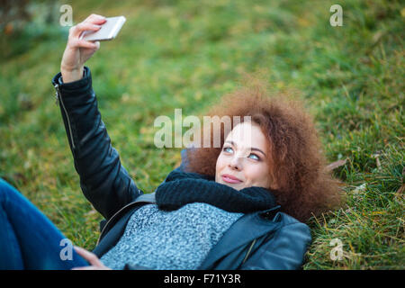 Porträt einer jungen Frau liegend auf dem grünen Rasen und Selfie Foto auf smartphone Stockfoto