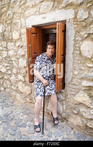 Ältere Frau saß auf einem Fensterbrett vor einem Haus in dem Dorf Mesta, Chios, Griechenland Stockfoto