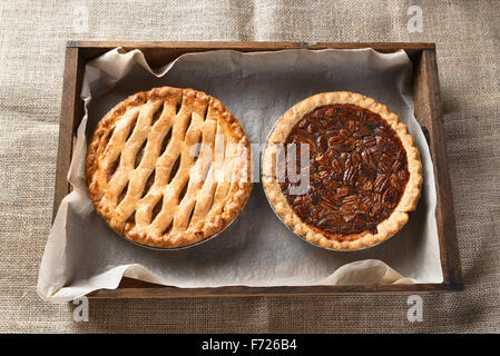 Erhöhte Ansicht eines Apfelkuchen und Pecan Pie in eine Holzkiste mit Backpapier ausgekleidet. Querformat auf ein Sackleinen Tabelle Gerinnsel Stockfoto