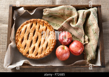 Vogelperspektive Blick auf einen frisch gebackenen Apfelkuchen und Äpfel in eine Holzkiste auf Sackleinen Oberfläche. Stockfoto