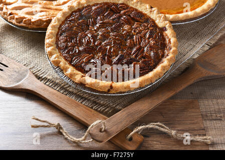 Nahaufnahme eines frisch gebackenen Pecan Pie mit Holz Geschirr und Sackleinen Tischdecke. Zwei weitere Torten im Hintergrund Thanksgiving Stockfoto