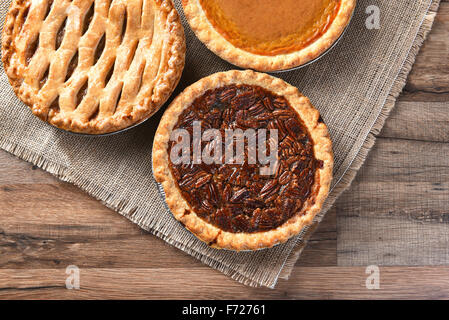 Drei frisch gebackene Torten Thanksgiving. Pecan Pie, Apfelkuchen und Kürbiskuchen, die von einem hohen Winkel auf eine Leinwand und Holz Oberfläche gesehen. Stockfoto