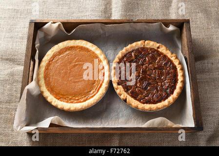 Erhöhte Ansicht von einem frischen gebackenen Kürbiskuchen und ein Pecan Pie in einer Holzkiste auf Sackleinen abgedeckt Tabelle für Thanksgiving fest. Stockfoto