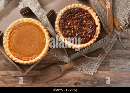 Ein Kürbis Pie und Pecan Pie in offenen Bäckerei-Boxen auf Leinwand und Holz Oberfläche mit Holz Utensilien. Stockfoto